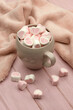 Lots of marshmallows in a big mug. Heart-shaped marshmallows in a mug on a pink background and a kitchen towel for coziness. Poster for interior.