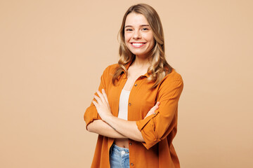Wall Mural - Side view young smiling Caucasian woman she wear orange shirt casual clothes hold hands crossed folded look camera isolated on plain pastel light beige background studio portrait. Lifestyle concept.