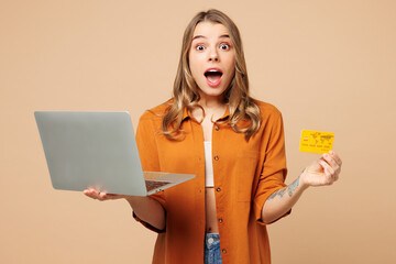 Canvas Print - Young shocked IT woman wears orange shirt casual clothes using mobile cell phone hold credit bank card shopping online order delivery book tour isolated on plain beige background. Lifestyle concept.