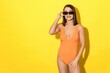 Stunning image captures the essence of a summer holiday in all its glory. A gorgeous young woman poses confidently in a trendy swimsuit against a bright yellow backdrop
