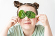 Little cute girl covered her eyes with spinach leaves. Concept of proper nutrition of children.