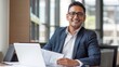 © liliyabatyrova - A smiling Latin American Man, businessman, Entrepreneur, Analyst, accountant, wearing a stylish suit, holding documents in his hands, working on a laptop, looking at a camera in a modern office.