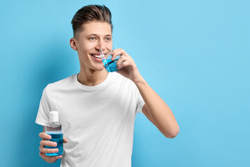 Canvas Print - Young man using mouthwash on light blue background, space for text