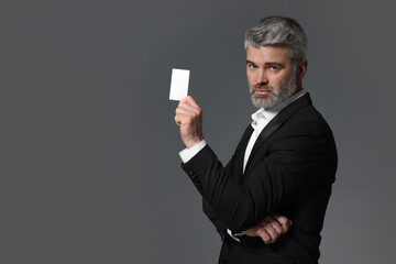 Canvas Print - Handsome businessman holding blank business card on grey background. Space for text