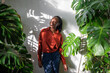 Relaxed African American woman stand in home garden enjoying houseplants. Carefree black female surrounded by indoor plants looks into distance. Plant lovers, mental health, slow life concept. 