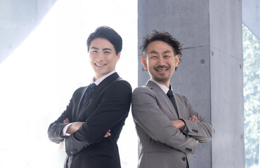 Wall Mural - Businessmen in suits, arms folded, backs to back, smiling Exec business image looking at goals and the future Looking at the camera