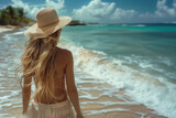 Fototapeta  - Donna al mare cammina in riva alla spiaggia con cappello di paglia