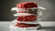 Stack of various raw meats separated with paper on a kitchen surface