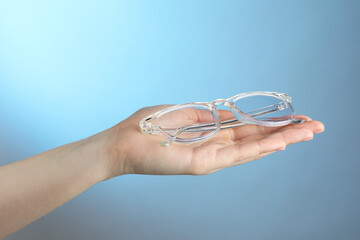 Poster - Woman holding glasses with transparent frame on light blue background, closeup