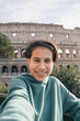 A Girl is smiling and taking a selfie in front of the Colosseum, concept of happiness and excitement as the girl enjoys her time in Rome
