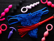 Bright blue panty, red whip and different sex toys over black wooden background