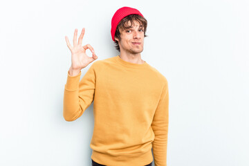 Wall Mural - Young caucasian man isolated on blue background winks an eye and holds an okay gesture with hand.