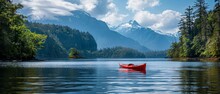 A Red Kayak Sits In A Calm Lake Surrounded By Snow-capped Mountains And Evergreen Trees.