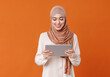 Beautiful overjoyed young smiling muslim woman in traditional religious hijab  reading great news on tablet.
