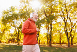 Fototapeta Przestrzenne - Happy senior man in headphones listening music while jogging outside in city park