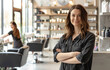 © Kien - A photo of beautiful salon owner standing with her arms crossed in front, wearing an apron and smiling at the camera while other stylist works on hair