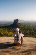 Man with backpack sitting on rock and looking at landscape. Beautiful scenery with Sigiriya rock. Solo traveler in Sri Lanka. .