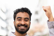 © Connect Images - A smiling man with curly hair is raising his fist in a gesture of success or celebration against a blurred urban background.