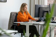 © Image Source - A woman is working at her desk with multiple monitors in a bright office environment.