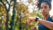 Focused Woman Checking Smartwatch During Outdoor Run. Athlete in training.