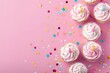 Delicious cupcakes with white frosting and colorful sprinkles on a pink background. Perfect for bakery or dessert concept