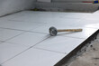 Tile floor under construction at interior. Include mallet tool, concrete mortar cement and white square ceramic tile. Finishing material for decor surface in bathroom, kitchen and shower room.