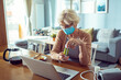 © Davor - Senior woman with face mask using laptop and feeling unwell at home