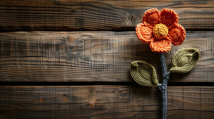 Wall Mural - Handcrafted Orange Crochet Flower with Green Leaves on Rustic Wooden Background
