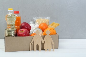 Wall Mural - Humanitarian aid for elderly people. Different donation food products and figures of senior couple on white wooden table. Space for text