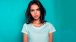 Portrait of an attractive young sad and unhappy brunette woman on a blue background with a copy space. A sweet, upset and offended girl in a simple white T-shirt.
