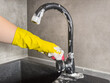 woman in yellow gloves with a sponge washes the kitchen faucet