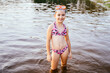 Happy preteen girl in swimsuit and mask in lake water standing knee-deep in water. Summertime children healthy vacation concept.