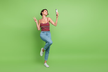 Canvas Print - Full length photo of attractive positive cute girl trendy clothes video live stream call v-sign isolated on green color background