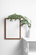 Vertical wooden frame mockup on white wall with natural eucalyptus twigs, copy space