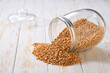 Raw organic wheats spill out of a glass storage jar on a white wooden table.