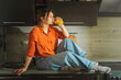 Beautiful young woman sitting on a tabletop with a glass of orange juice.