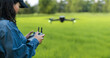 A female farmer wearing a hat stands and controls a drone in a green wheat field. Modern technology in digital agriculture