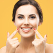 Happy excited woman pointing show white teeth smile. Face portrait of optimistic girl, isolated against yellow background. Optimism or Dental Health Care ad concept. Square image.