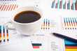 Cup of coffee, ballpen and financial chart showing different production or sales statistics. Business