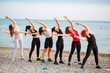 Row of adult Caucasian woman training at beach. Outdoor activity. Concept of fitness and yoga