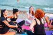 Yoga class. Group of young-adult multi-racial women are sitting on sports mats on wild beach and talking to each other. Concept of female circle of communication and support