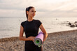 Portrait of young pretty Caucasian woman holds sport mat and posing on beach. Copy space. Concept of wellness