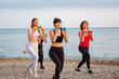 Outdoor yoga and fitness. Three adult fit women are training with dumbbells on wild pebble beach. Concept of sports lifestyle