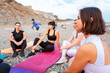 Group of young-adult multi-racial women are sitting on sports mats on wild beach and talking to each other. Concept of female circle of communication and outdoor yoga class