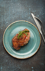 Canvas Print - Delicious roasted duck breast fillet with golden crispy skin, with pepper and rosemary, top view on ceramic blue plate, rustic concrete rustic background.