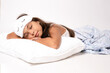 Beautiful child girl wearing sleep mask and pajama standing over isolated white background sleeping tired dreaming and posing with hands together while smiling with closed eyes.