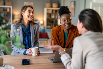 Wall Mural - Team of three business women working in an office. Three happy females smiling while having a discussion. Group of modern females entrepreneurs collaborating on a new project in an office.