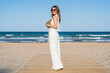 Elegant woman with sunglasses and white dress posing on the beach on a sunny day