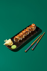 Sticker - An exquisite Unagi roll, topped with Tobiko caviar and packed with shrimp, elegantly presented on a black plate alongside chopsticks, wasabi, and ginger. The setting features a deep green backdropю