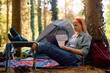 Young woman surfing net on laptop while camping in woods.